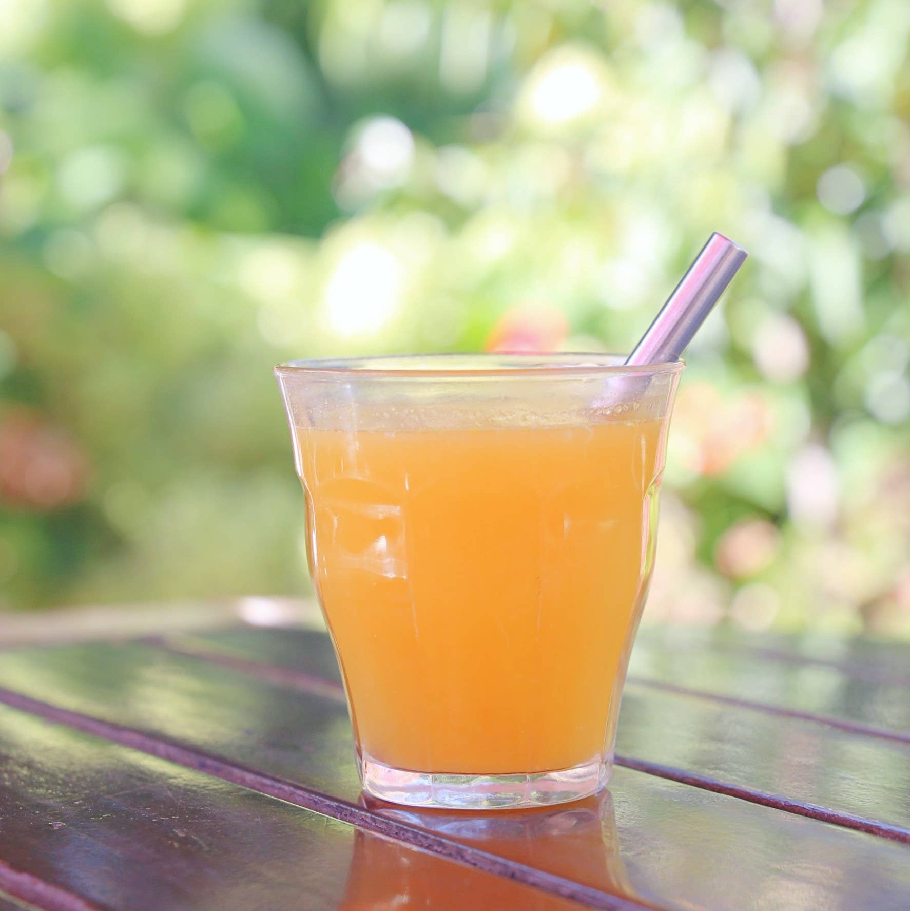 Leafera- Glass of orange juice with a straw on a table outdoors