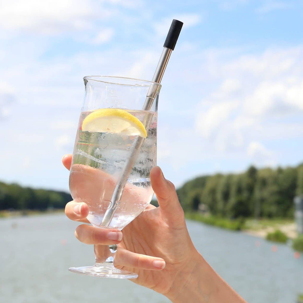 Leafera- Hand holding a glass of lemon water with a straw, outdoors by a lake.
