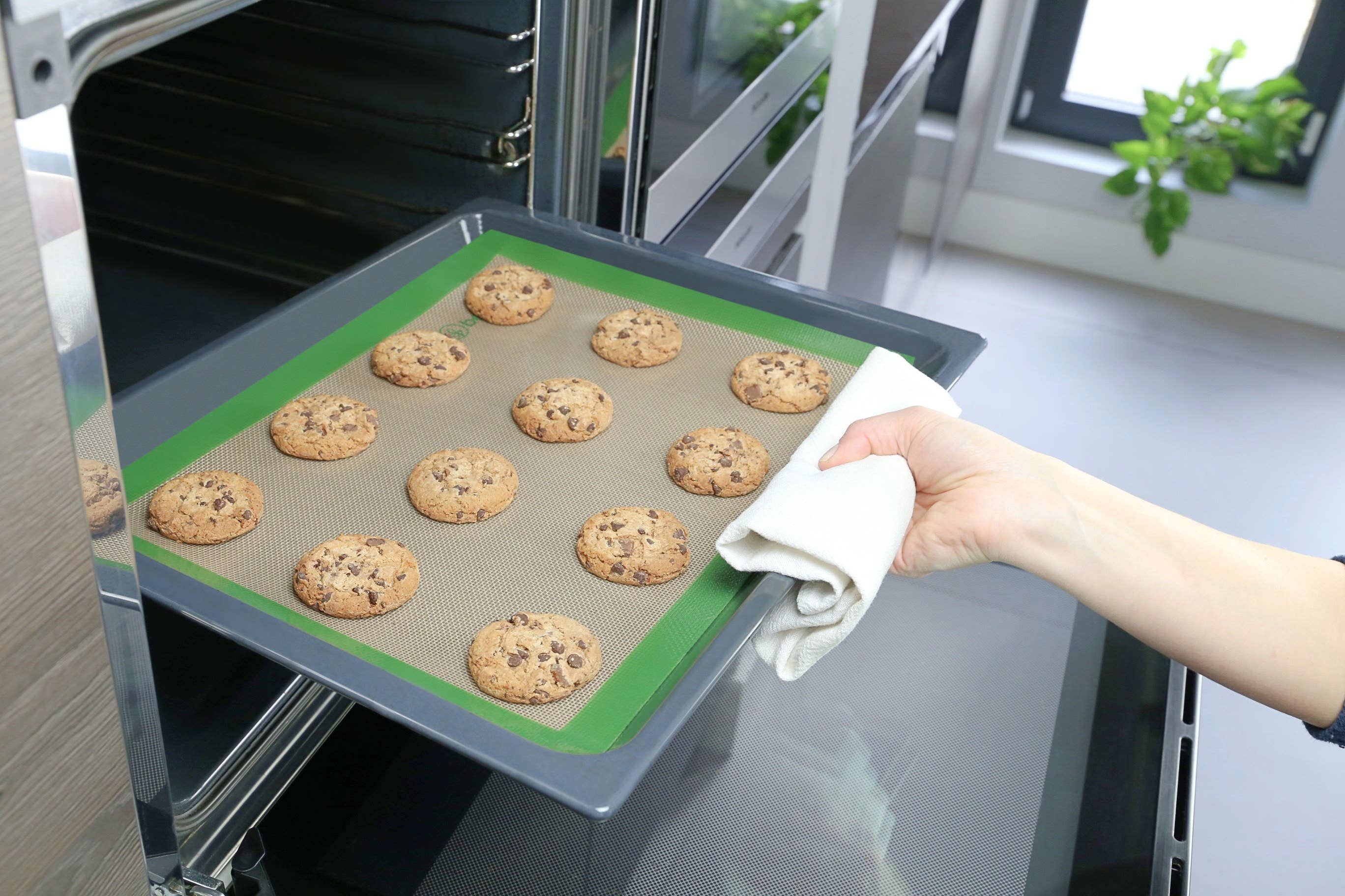 Leafera- Person removing a tray of cookies from an oven using a silicone baking mat.